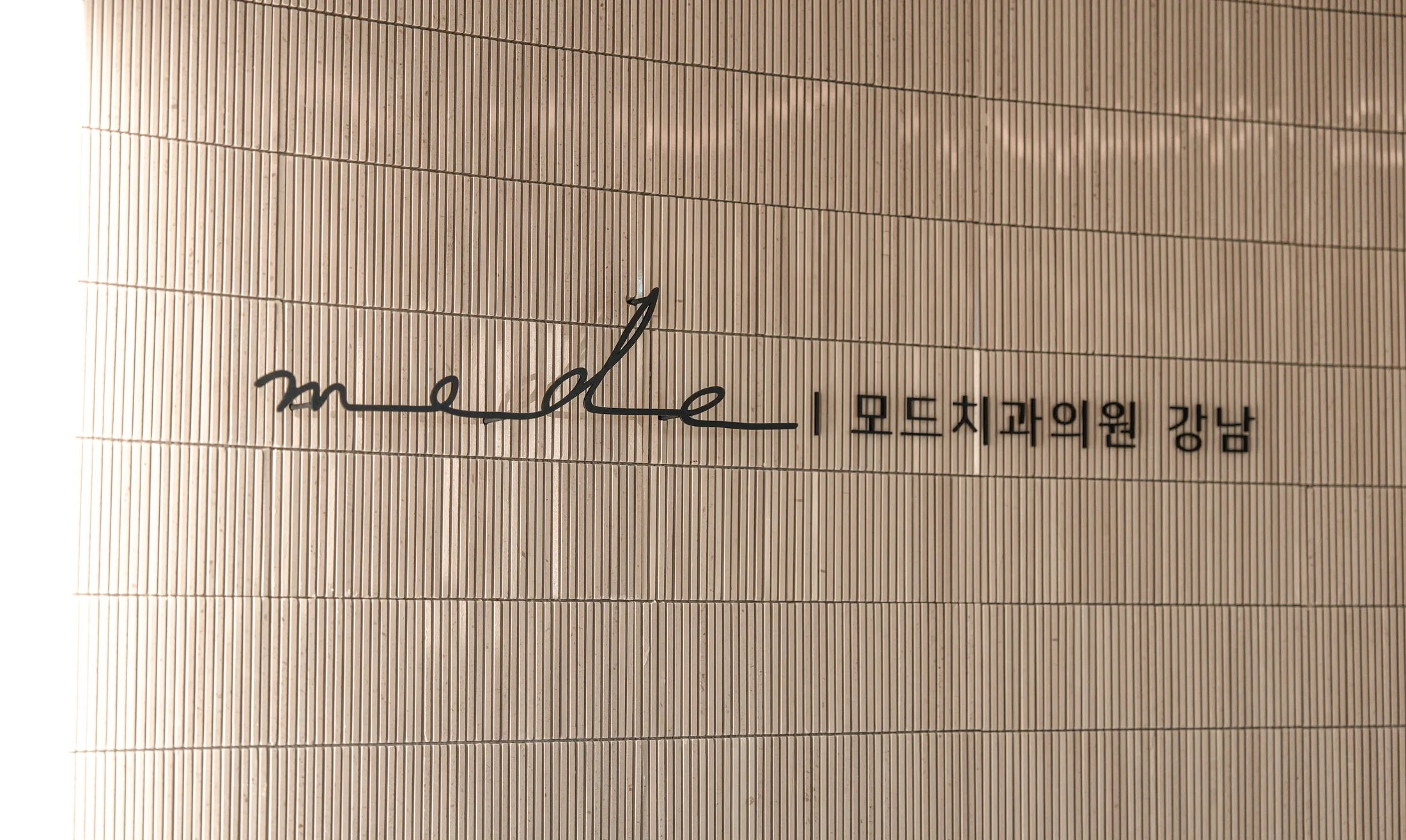 베이지색 타일 벽면의 모드치과의원 강남 로고